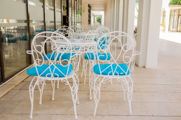 Güneşli verandada mavi yastıklı beyaz teras sandalyeleri. Açık hava zarafeti, Akdeniz eğlencesi ve yaz konukseverliği tasarımı.