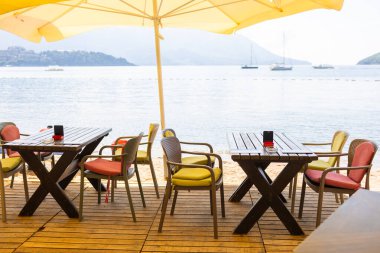 Deniz manzaralı açık bir kafe ve boş hasır sandalyeler. Akdeniz bölgesinde kıyı rahatlığı, yaz turizmi ve deniz kıyısında akşam yemeği..