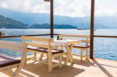 Deniz manzaralı açık bir kafe ve boş hasır sandalyeler. Akdeniz bölgesinde kıyı rahatlığı, yaz turizmi ve deniz kıyısında akşam yemeği..