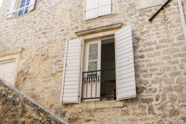 Kırsal pencere, açık ahşap panjurlar ve taş duvarda saksı bitkileri. Akdeniz cazibesi, bahçe işleri ve rahat mimari..