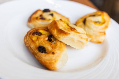 Otel kahvaltısı sırasında beyaz tabakta servis edilen üç kuru üzümlü pasta. Sabah tatlıları, tatlı pastane atıştırmalıkları ve zarif masa hazırlama konsepti..