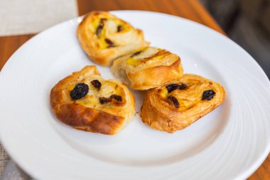 Otel kahvaltısı sırasında beyaz tabakta servis edilen üç kuru üzümlü pasta. Sabah tatlıları, tatlı pastane atıştırmalıkları ve zarif masa hazırlama konsepti..