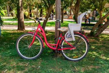 Çocuk koltuğu olan kırmızı bir bisiklet. Aile yaşam tarzı, çevre dostu ulaşım ve yeşil açık alanlarda şehir eğlencesi.
