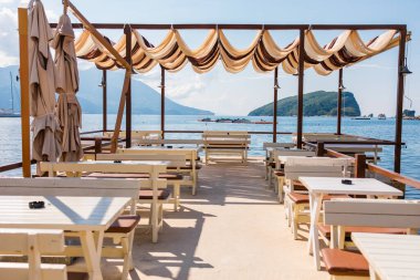 Gölgeli tepe örtüsü ve panoramik ada manzaralı deniz kenarı restoran terası. Yaz tatili, konukseverlik ve kıyı turizmi konsepti