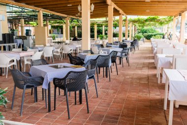 Masaları ve tahta sandalyeleri olan modern restoran terası. Sıradan yemekler, rahat bir ortam ve yaz misafirperverliği deneyimi.