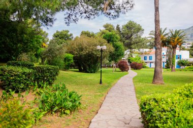 Bir yazlık oteldeki huzurlu bahçe yolu. Yeşillik, palmiye ağaçları ve Akdeniz kıyısındaki huzurlu tatil atmosferi
