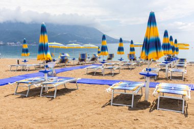 Mavi şemsiyeli ve şezlonglu bir sahilde sakin bir sabah. Sahil tatili, yaz tatili ve huzurlu sahil turizmi.