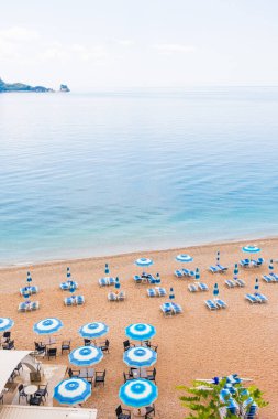 Mavi şemsiyeli ve şezlonglu bir sahilde sakin bir sabah. Sahil tatili, yaz tatili ve huzurlu sahil turizmi.
