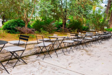 Yapraklı park ortamında açık kafe koltuklar. Yeşilliklerle çevrili rahat kentsel yaşam tarzı ve sosyal toplanma alanı