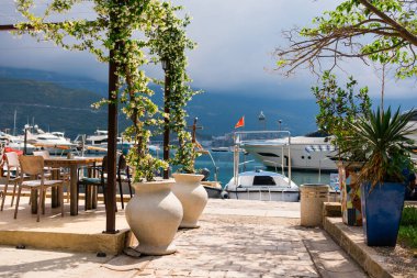 Çiçekli sarmaşıklar ve lüks yatların deniz manzaralı sıcacık kafe terası. Açık hava eğlencesi, Akdeniz atmosferi ve huzurlu tatil havası.