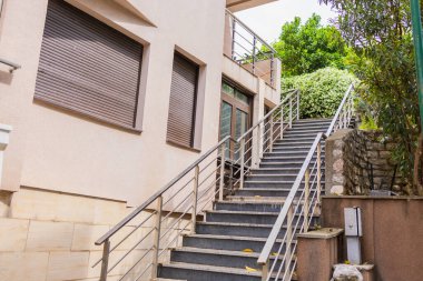 Siyah metal korkuluklu ve yeşil çalılıklı taş merdiven. Temiz hatları ve doğal dokuları olan şehir bahçesi mimarisi.