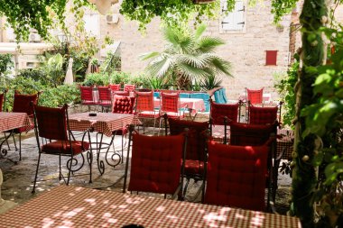 Akdeniz avlusunda kırmızı kareli masa örtüleri olan büyüleyici bir açık hava kafesi. Yaz atmosferi, konukseverlik ve huzurlu yemek..