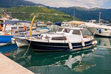 Motorlu tekne dağ arkaplanlı manzaralı bir marinada demirlemiş. Sahil yaşam tarzı, deniz eğlencesi ve deniz kıyısında yaz turizmi.