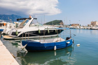 Motorlu tekne dağ arkaplanlı manzaralı bir marinada demirlemiş. Sahil yaşam tarzı, deniz eğlencesi ve deniz kıyısında yaz turizmi.