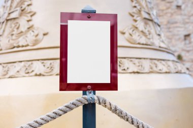 Blank sign with red border in front of ornate bell. Heritage tourism, information signage, and museum atmosphere.