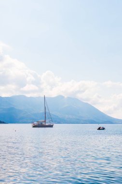 Yelkenli, yumuşak güneş ışığı altında dağlık kıyı şeridine demir attı. Sahil seyahati, deniz eğlencesi ve manzaralı yaz kaçışı.