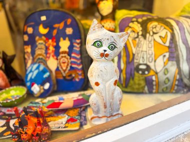 Renkli hediyelik eşyalar ve sergilenen ahşap kedi heykelciği olan bir dükkan penceresi. El yapımı ürün ve yerel pazar tarzında yaratıcılık, kültür, sanat ve dekorasyon