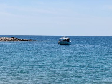 Kayalık bir kıyıya yakın sakin bir denizde yüzen küçük bir tekne. Huzur, denizcilik hayatı ve sahil şeridinde rahatlık.