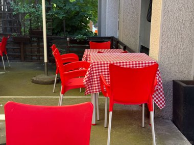 Kırmızı plastik sandalyeler ve açık kafe terasında kareli bir masa. Sokak yemekleri, günlük atmosfer ve günlük yaşam tarzı.