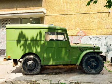 Sarı duvarın yanına park edilmiş eski yeşil bir araç. Klasik ulaşım, sokak kültürü ve şehir tarihinin temsili