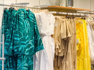 Mevsimlik moda elbiseleri ve tekstil ürünleriyle butik dükkanındaki askılarda sergilenen kıyafet koleksiyonu. Perakende satış, giysi sunumu, alışveriş yaşam tarzı ve modern tarz.