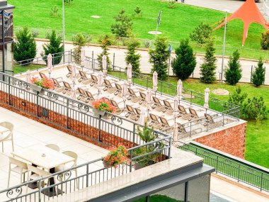 Bir tesiste sergilenen şezlonglar, şemsiyeler ve dekoratif çiçeklerle dolu teras. Konukseverlik, rahatlama, tatil yaşam tarzı ve modern tasarımı sembolize eden turizm