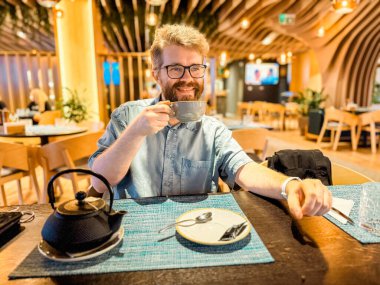 Restoran masasında sıcak çay yudumlayan bir adam, modern iç mekan ve sıcak aydınlatma. Yaşam tarzı, rahatlama, rahatlama, ve konukseverlik konsepti rahat atmosfer ve keyif