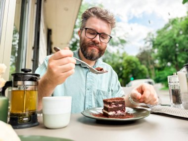 Açık kafede elinde çaydanlık ve fincanla pasta yiyen bir adam. Günlük rahatlama ve otantik yemek zevkinin yaşam tarzı ve boş yemek deneyimi