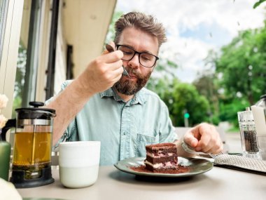 Açık kafede elinde çaydanlık ve fincanla pasta yiyen bir adam. Günlük rahatlama ve otantik yemek zevkinin yaşam tarzı ve boş yemek deneyimi