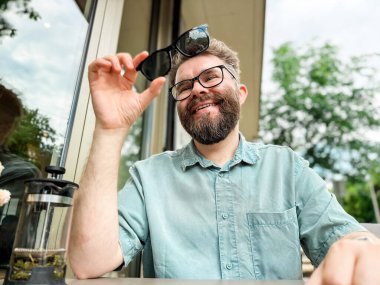 Açık kafe masasında güneş gözlüğü takan bir adam gülümsüyor. Güneş gözlüklü manyetik gözlük.