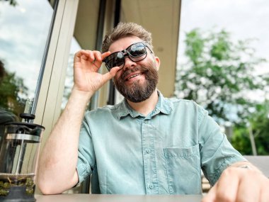 Güneş gözlüklerinde manyetik şarjör olan gözlük. Dışarıdaki kafe masasında güneş gözlüğü takan bir adam gülümsüyor..