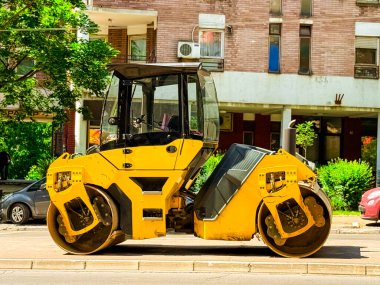 Şehir sokağına park edilmiş sarı paten makinesi. Modern şehirde asfalt sıkıştırma, altyapı geliştirme ve yol bakımında kullanılan ağır ekipmanlar