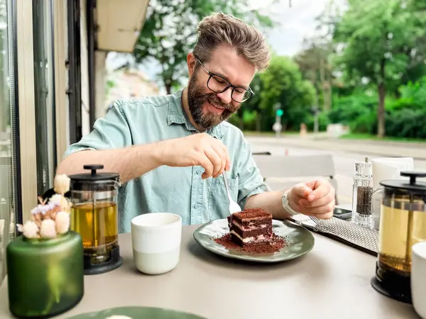 Açık kafede elinde çaydanlık ve fincanla pasta yiyen bir adam. Günlük rahatlama ve otantik yemek zevkinin yaşam tarzı ve boş yemek deneyimi