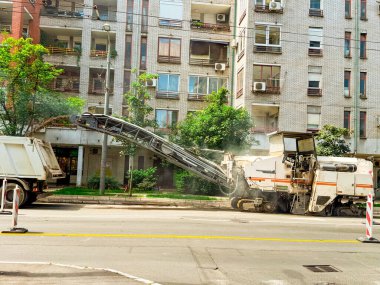 Asfalt değirmen makinesi şehir caddesinde enkazı kamyona yüklüyor. Altyapı geliştirme ve belediye karayolu bakım projesi için ağır ekipman operasyonu