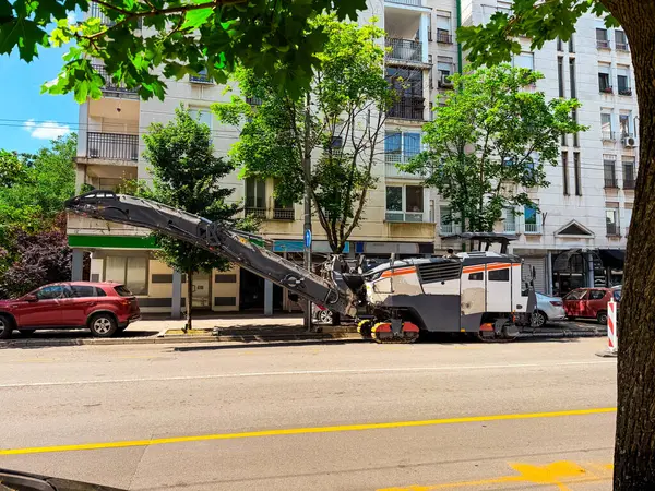 İnşaat kamyonu ve asfalt değirmen makinesi apartmanların yanındaki caddede çalışıyor. Altyapı onarımı modernizasyonu, kentsel gelişimi ve yol bakımını sembolize eder