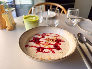 Bir kase yulaf lapası, ahududu sosu ve fındık, kafenin içinde servis ediliyor. Sağlıklı kahvaltı, dengeli beslenme ve sağlıklı yaşam tarzı..