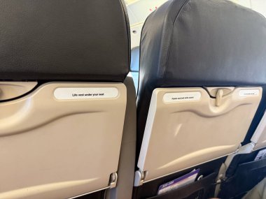 Uçak kabini içinde emniyet etiketleri olan koltuklar. Uçak yolculuğu, yolcu güvenliği ve havacılık detayları.
