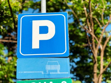 Şehirdeki metal bir direkte beyaz P harfli mavi park levhası var. Taşımacılık, düzenleme ve kamu altyapısı araç yönelimini, hukuku ve şehir hareketliliğini güvence altına alıyor