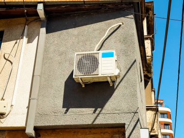 Görünür kabloları olan gri bir binanın dış duvarına bağlı bir havalandırma ünitesi. Kentsel iklim kontrolü ve ev konforunu temsil eden soğutma aygıtı, altyapı ve teknoloji