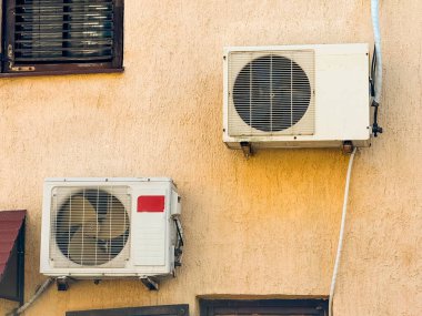 Vantilatör kapaklı bir binanın duvarına yerleştirilmiş iki havalandırma ünitesi. Soğutma sistemi, ev altyapısı ve teknoloji kentsel konfor ve iklim düzenlemesi sağlıyor