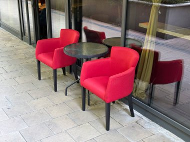 Cam duvarlı, kafenin terasına küçük yuvarlak bir masa konmuş iki kırmızı döşemeli sandalye. Konukseverlik, yaşam tarzı ve yemek ortamı konfor, eğlence ve modern tasarımı yansıtıyor