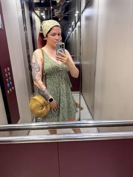 Çiçekli bir yaz elbisesi içinde aynalı selfie çeken bir kadın. Günlük çevrede moda, kadınlık ve günlük yaşam tarzı