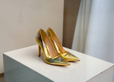 Mağaza vitrininde beyaz bir stantta sergilenen altın işlemeli yüksek topuklu ayakkabılar. Moda, zarafet ve yaşam tarzı perakende, tarz ve tüketici kültürü yoluyla yansıtılır.