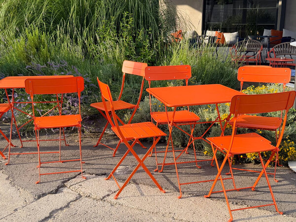 Red metal chairs and a tables on an outdoor cafe terrace. Street dining, casual atmosphere and everyday urban lifestyle