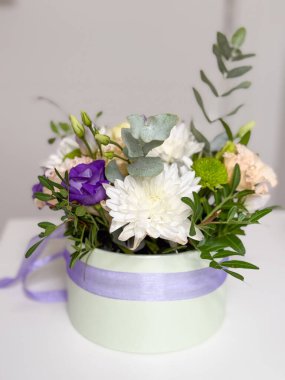 Beyaz kasımpatı, mor lisianthus, şeftali çiçeği ve yeşillik içeren bir pastel kutuda zarif bir çiçek aranjmanı. Hediye, kutlama ya da düğün dekorasyonu için mükemmel..