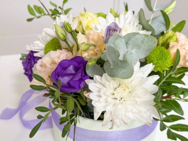 Çiçek aranjmanı gül, kasımpatı ve leylak kurdeleyle bağlanmış yuvarlak hediye kutusunda lisianthus. Kutlama buketi, romantik dekorasyon, zarafet, şefkat, şenlik, iç güzellik ve uyum.