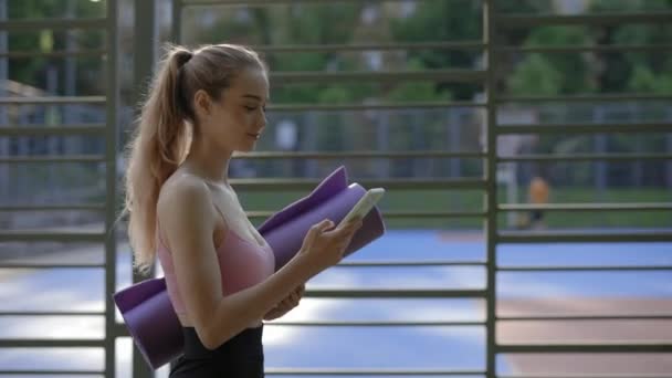 Giovane Donna Sta Fare Yoga Tenendo Tappetino Yoga Utilizzando Smartphone — Video Stock