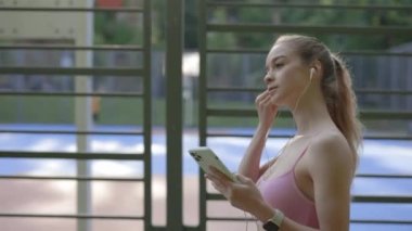 Yan gören bayan sporcu kulaklığı kulağına takıyor telefonu tutuyor ve koşmaya başlıyor. Spor fitness teknolojisi egzersizi