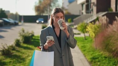 Alışveriş yaptıktan sonra eve giden, kahve içen, telefonları kaydıran bir kadın. Yürüyen bir bayan, akıllı telefon kullanıyor. Satın almadan sonra müşteri