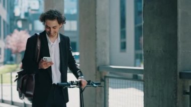 İş adamı iş merkezine resmi siyah takım elbiseyle gidiyor. Sosyal medyadaki iş sohbetlerine cevap veren elektrikli bisikleti taşıyor. Erkek patron iş yerinin yakınında akıllı telefon kullanıyor.